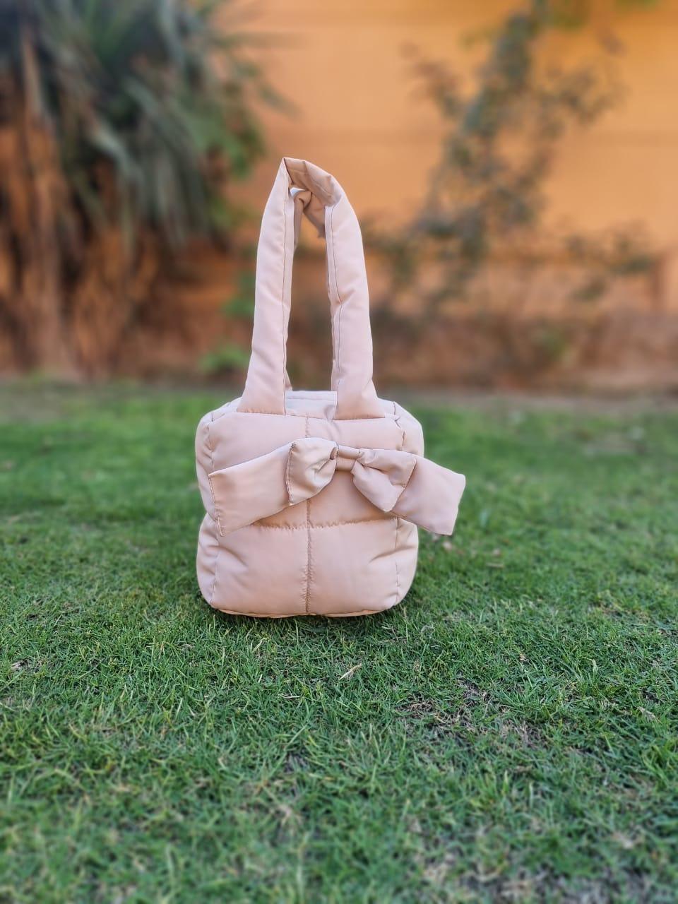 Beige handmade cotton beauty case with bow detail, displayed outdoors on green grass