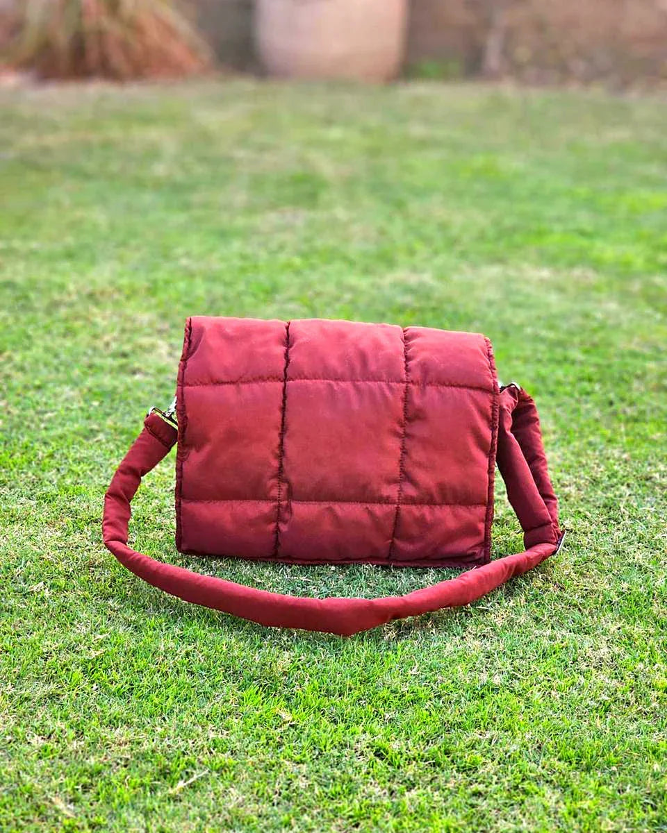 Handmade quilted maroon cotton shoulder bag on green grass outdoors