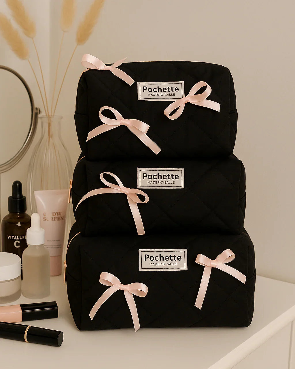 Stacked black quilted beauty cases with pink bows on a vanity, surrounded by skincare and makeup items
