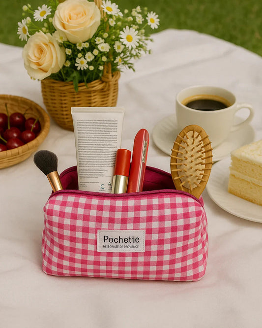 Pink gingham beauty case with cosmetics on a picnic setup, flowers and coffee in background