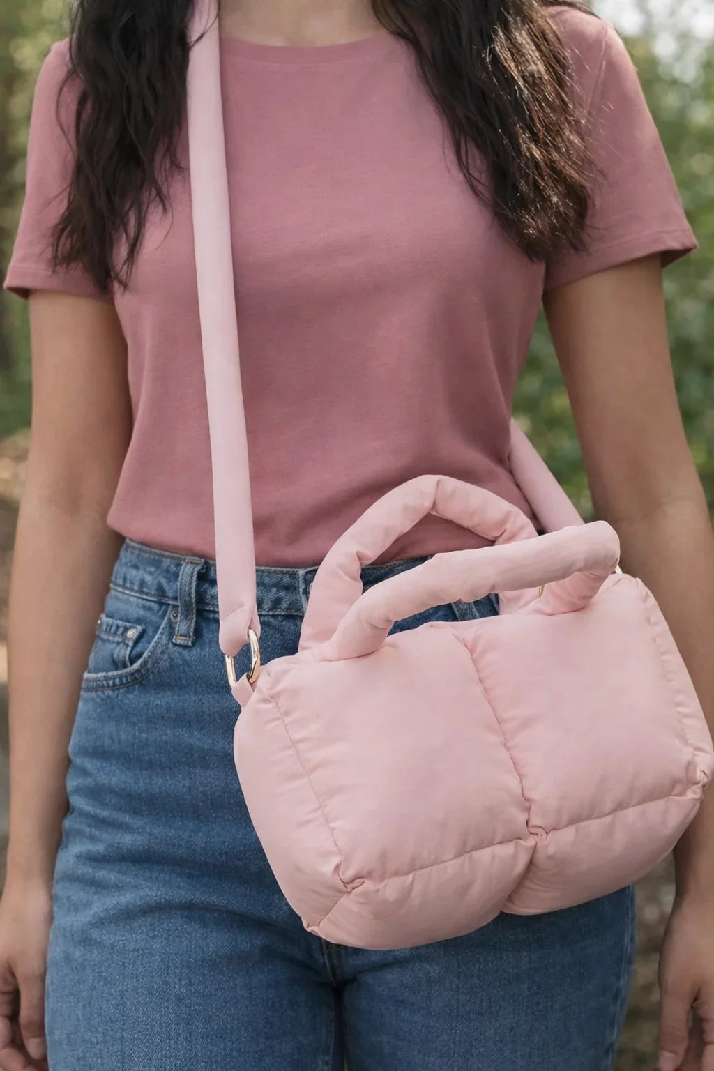 Light pink puffer quilted crossbody bag with handles, worn over shoulder outdoors
