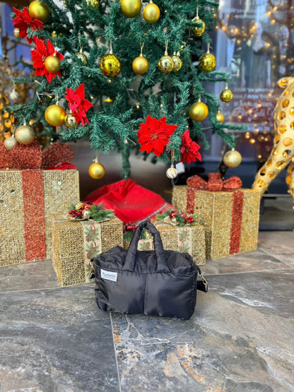 Black puffer quilted crossbody bag set on stone floor with Christmas tree and gift boxes.