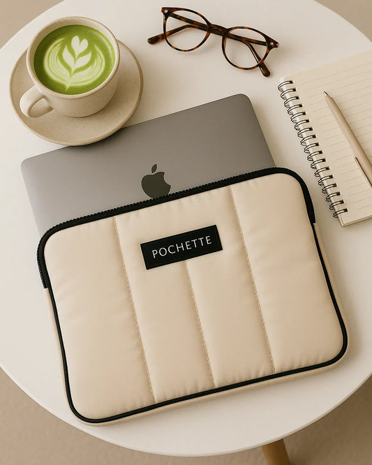 Quilted padded laptop sleeve in cream on table with laptop, notebook, glasses, and matcha latte