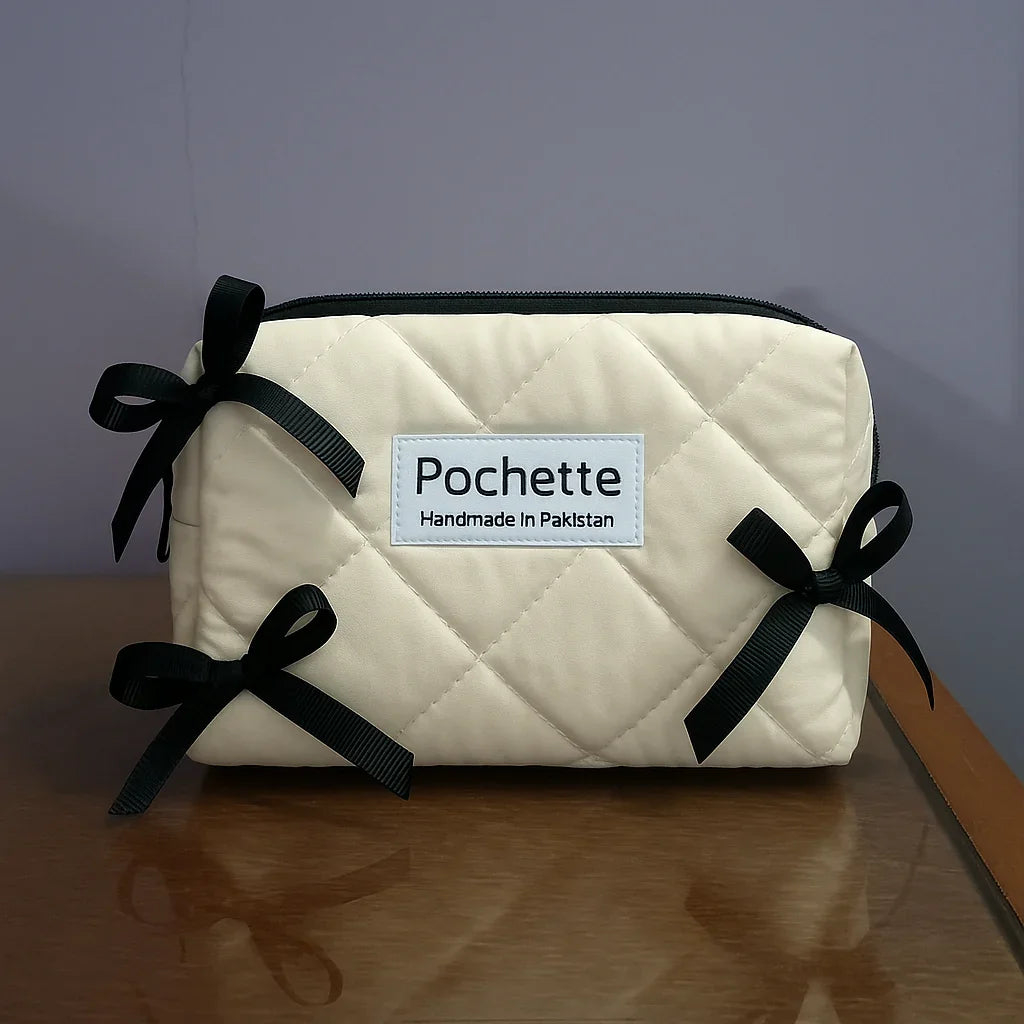 Quilted cream beauty case with black bows and label, handmade cotton accessory on table