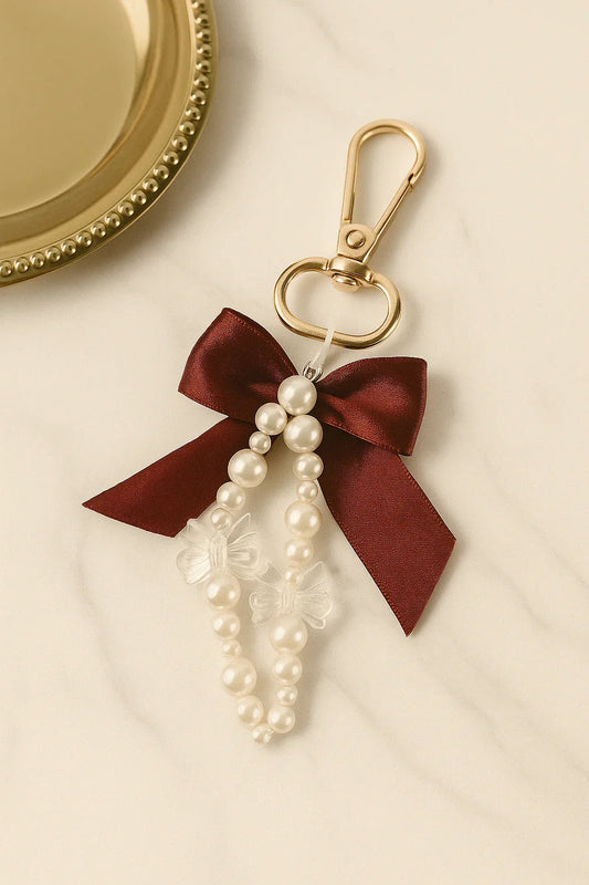 Gold keychain with burgundy satin bow, pearl beads, and clear butterfly charms on marble surface