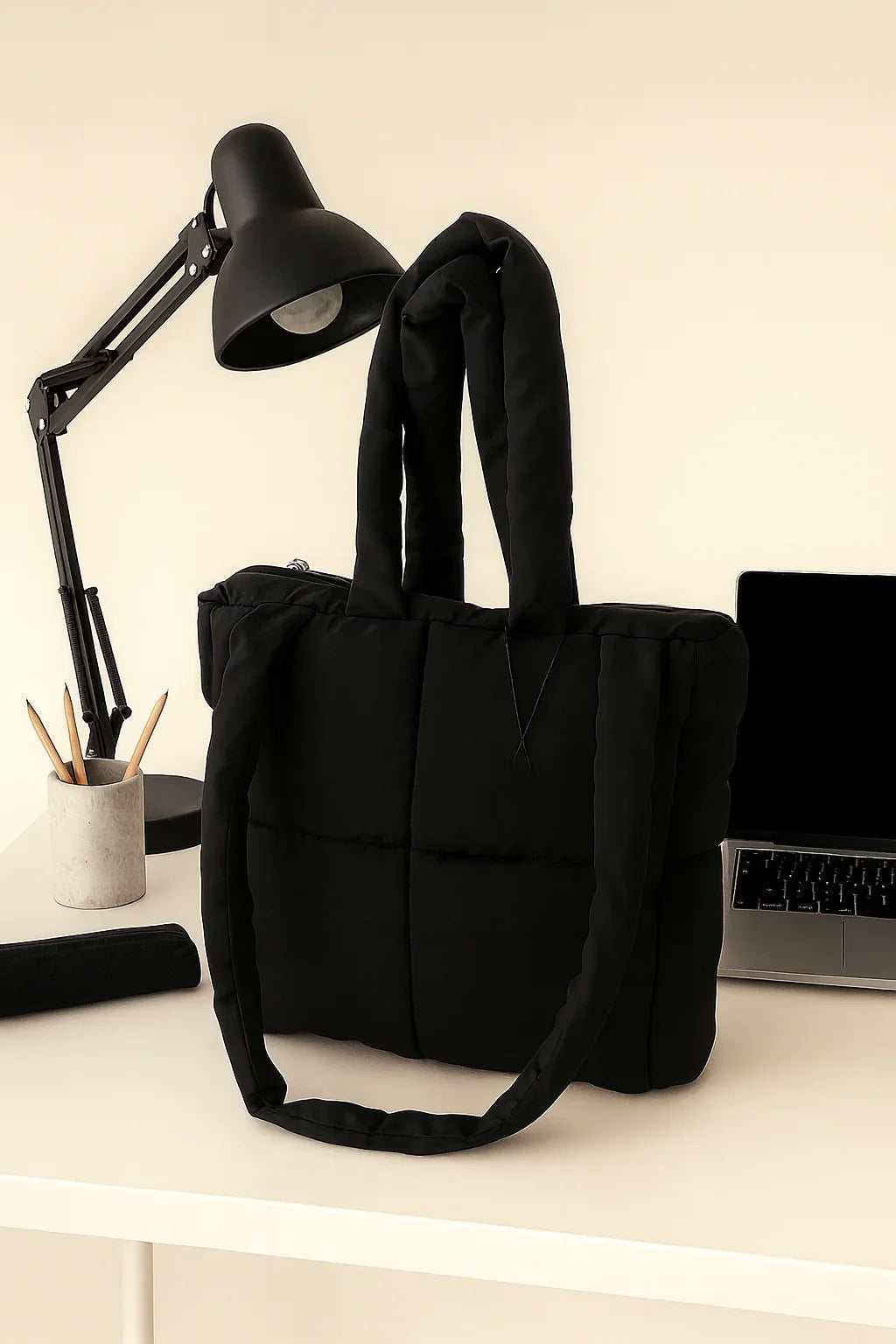 Black quilted cotton tote bag on white desk with lamp, pencils, and laptop