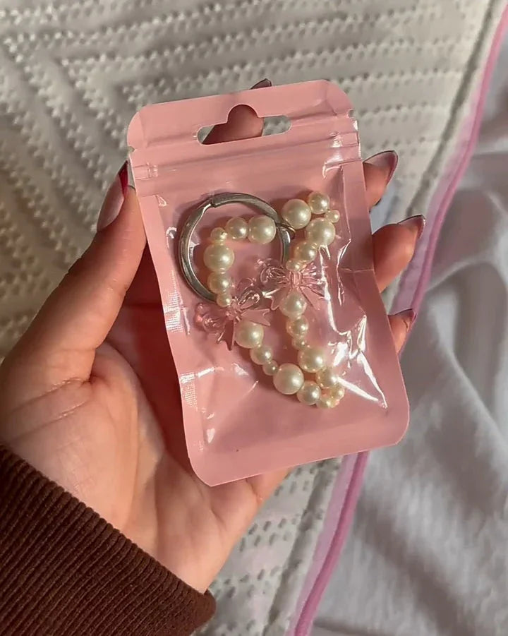 Hand holding a pearl beaded heart keychain in clear pink packaging on a textured bedspread